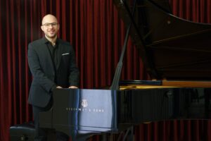 Angelo Morelato, insegnante di pianoforte, sorridente accanto al pianoforte a coda